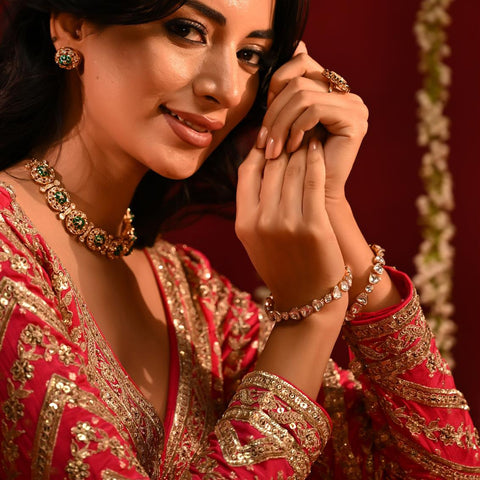 Woman in traditional red and gold outfit with jewelry against a decorative background